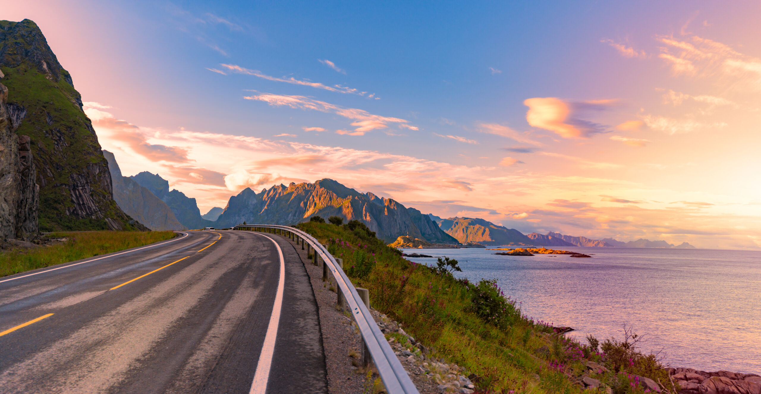 Panorama of empty winding country road in Norway, Europe, Scandinavia. Auto travel on sunset. Blue sky with clouds and mountains. Lofoten islands.
