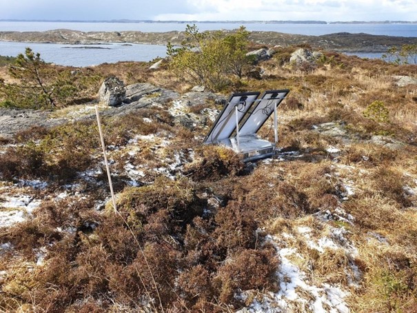Coastal landscape with sea, islets and vegetation together with a small land-based listening station that looks like two panels and a small box. Photo
