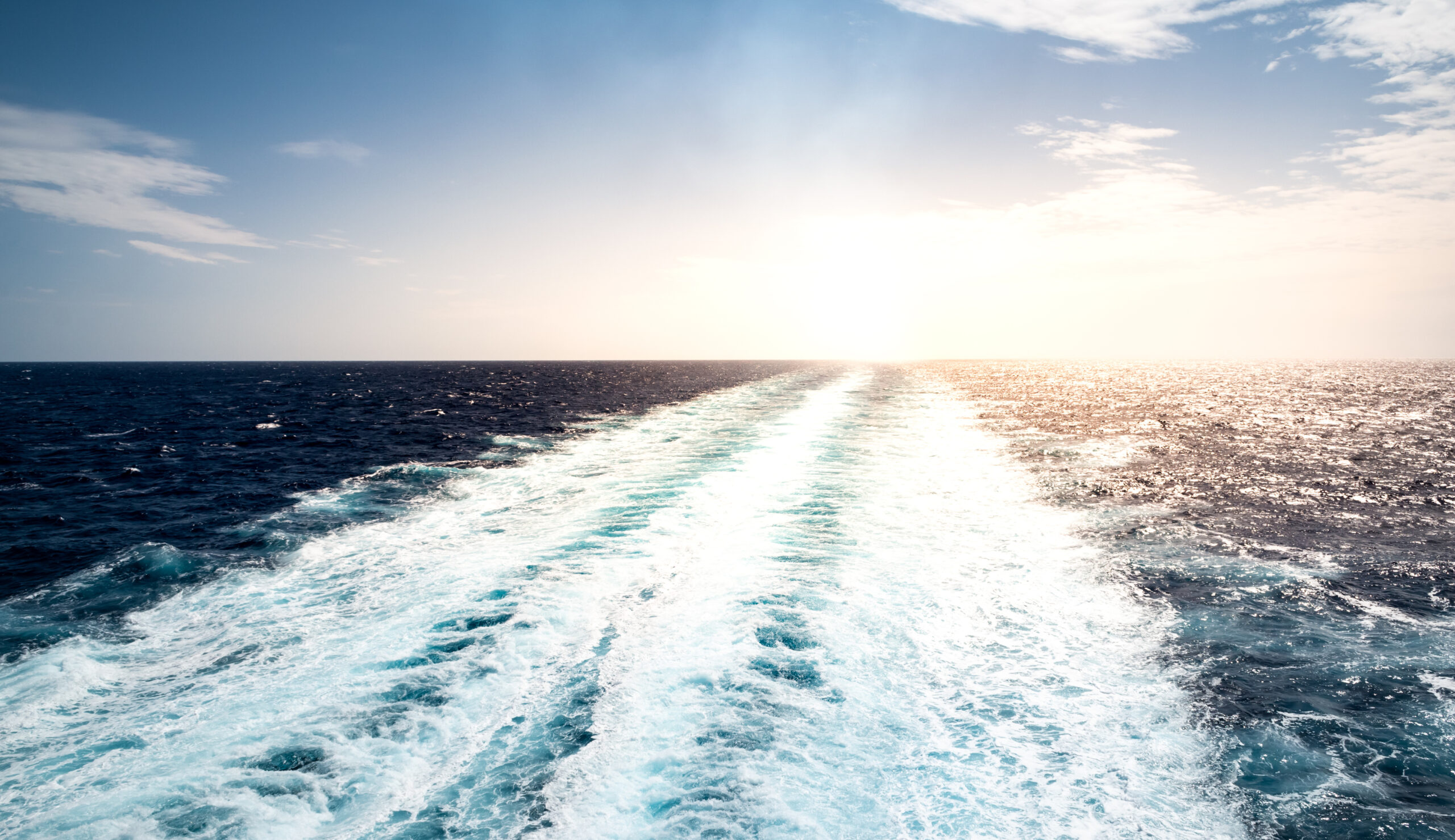Skummende spor av seilende cruiseskip på Middelhavet en sommerferiedag. Ingen mennesker. Fredelig havlandskap med små bølger, rolig hav og sol.