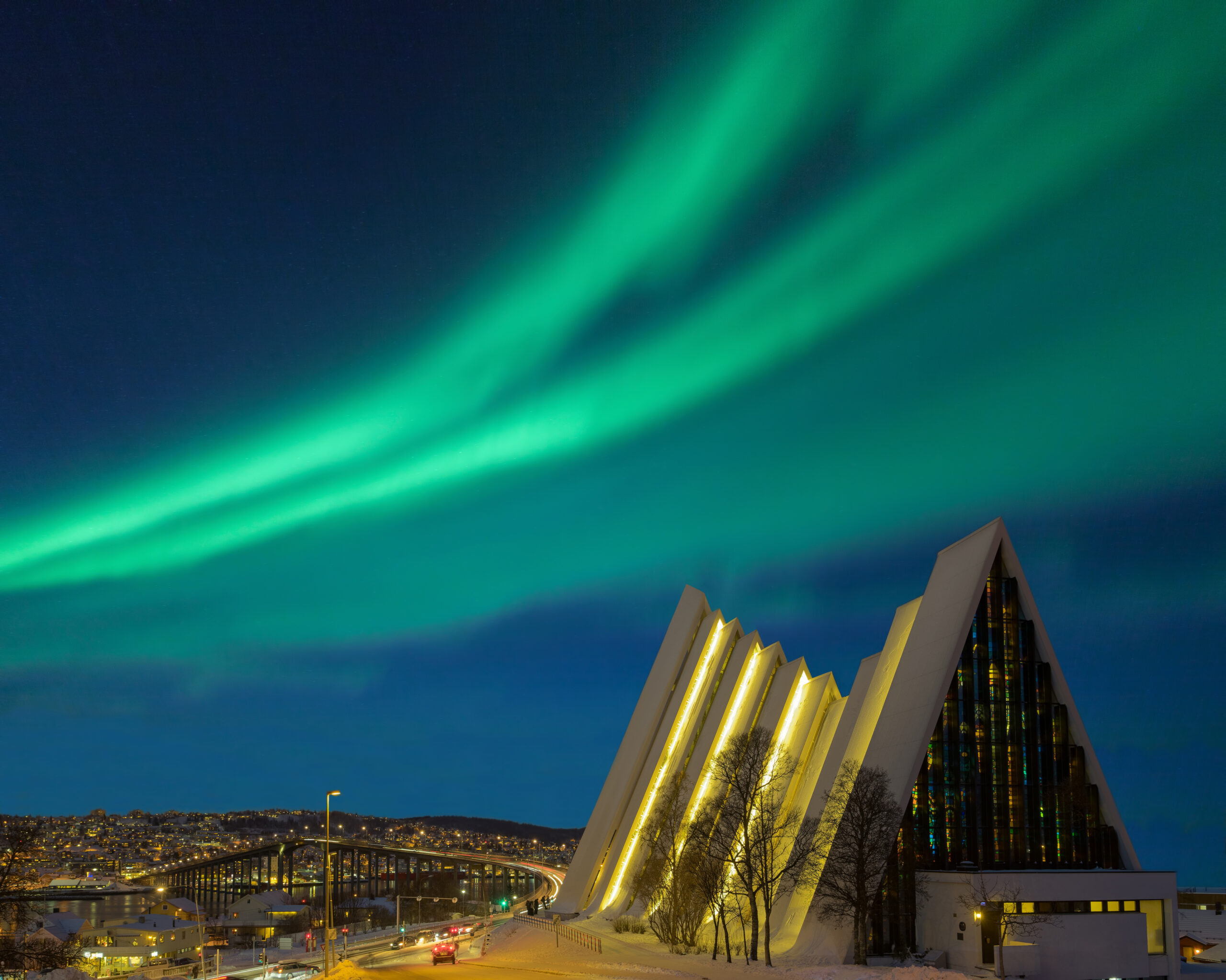 Opplyst Tromsø domkirke om natten med vakre, grønne former av nordlys