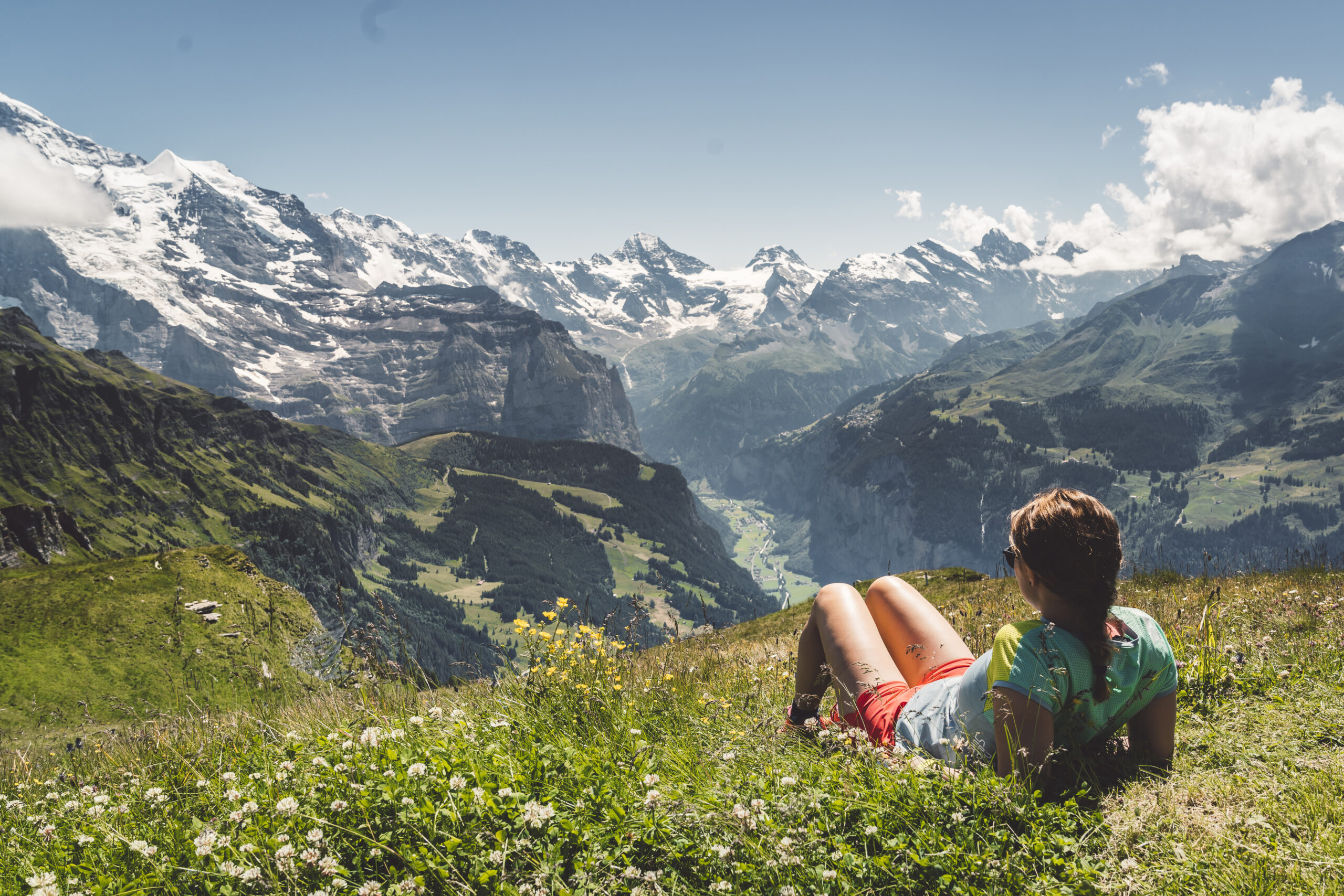 Woman hiker laying on a field up in the mountains looking at the view of Swiss Alps on a sunny day. Photo.