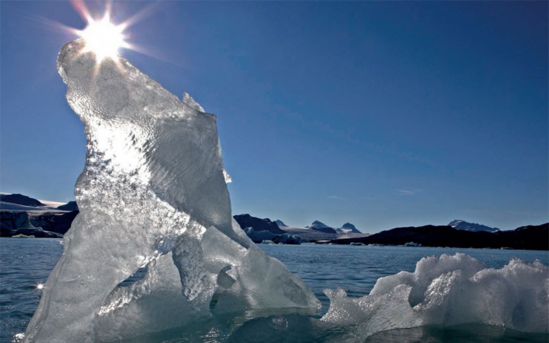En isfigur i havet med snødekte fjell i bakgrunnen. Foto.